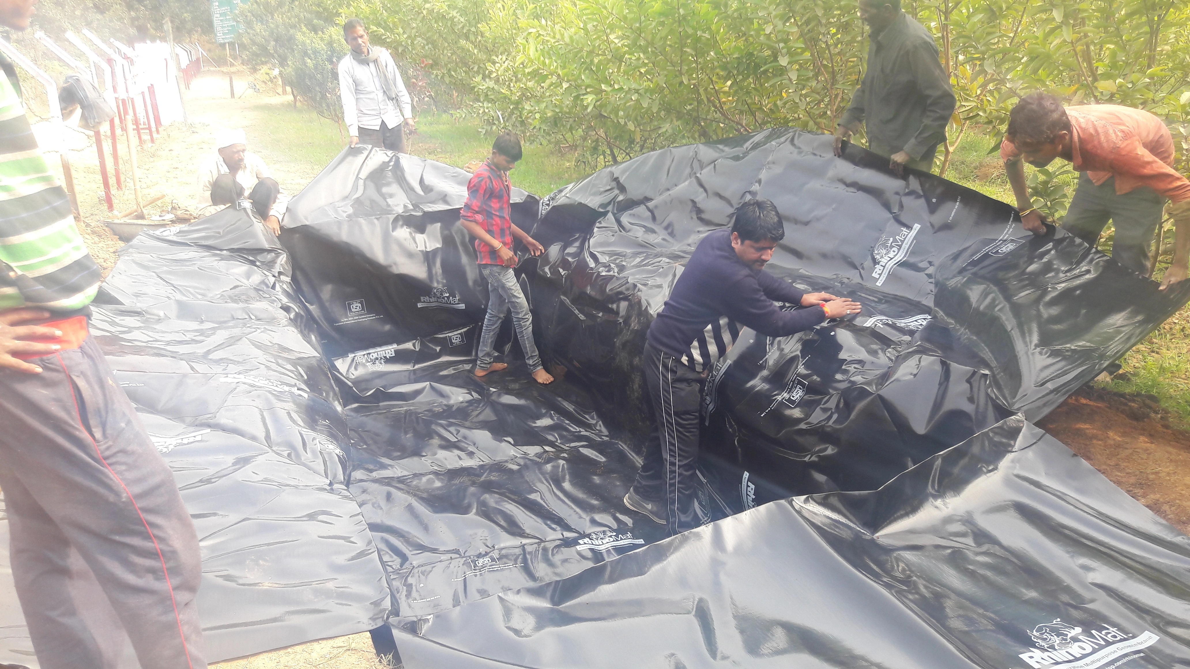 Several people work together to spread and adjust a large custom prefabricated protective packaging pond.